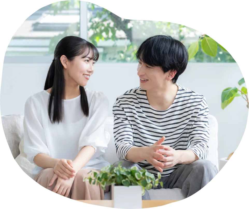 大きな窓のある明るいリビングで、ソファに座る若い男女が向かい合い談笑している様子