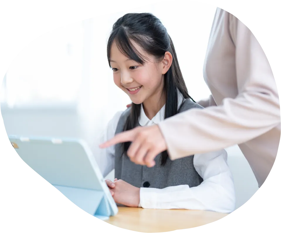明るい室内で、笑顔の女の子がタブレットを見ながら、大人が画面を指差して示している様子