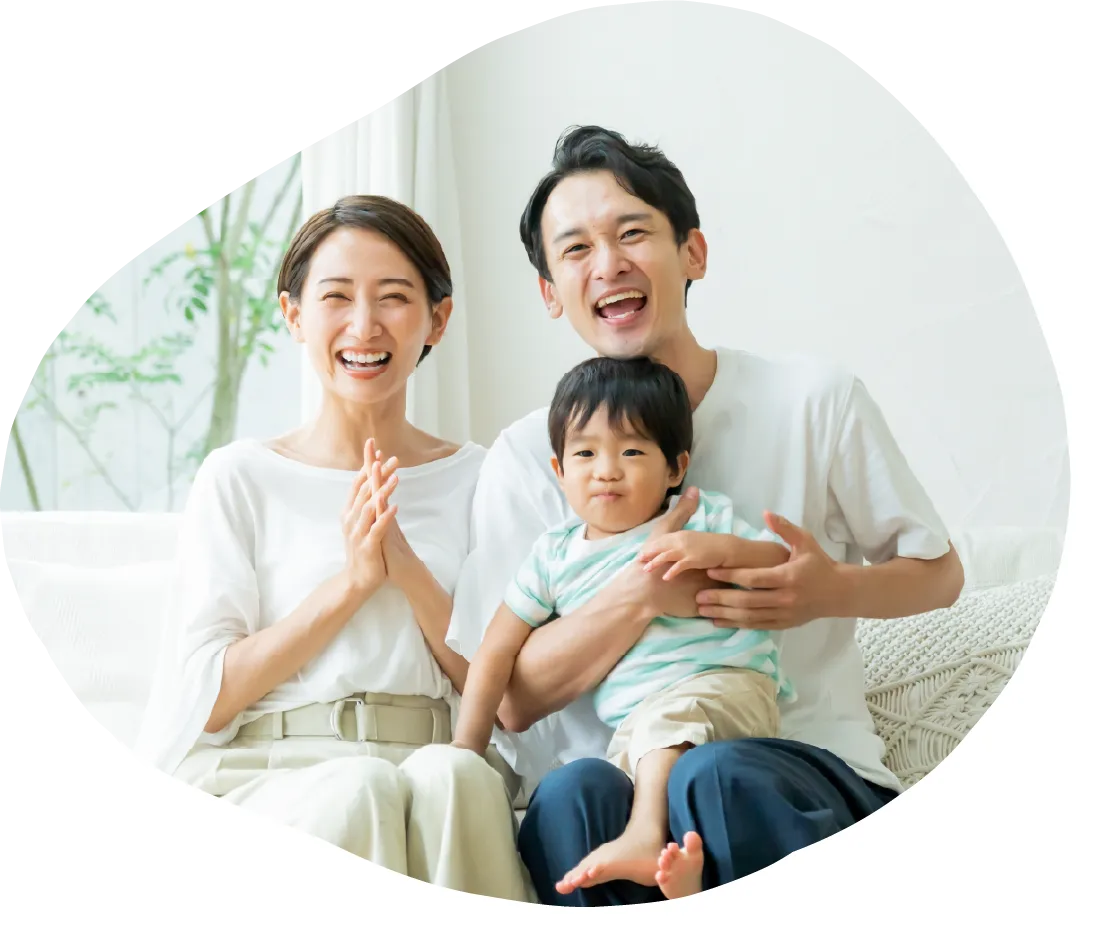 明るい室内のソファで、親子三人が笑顔で寄り添い、くつろいで過ごしている様子